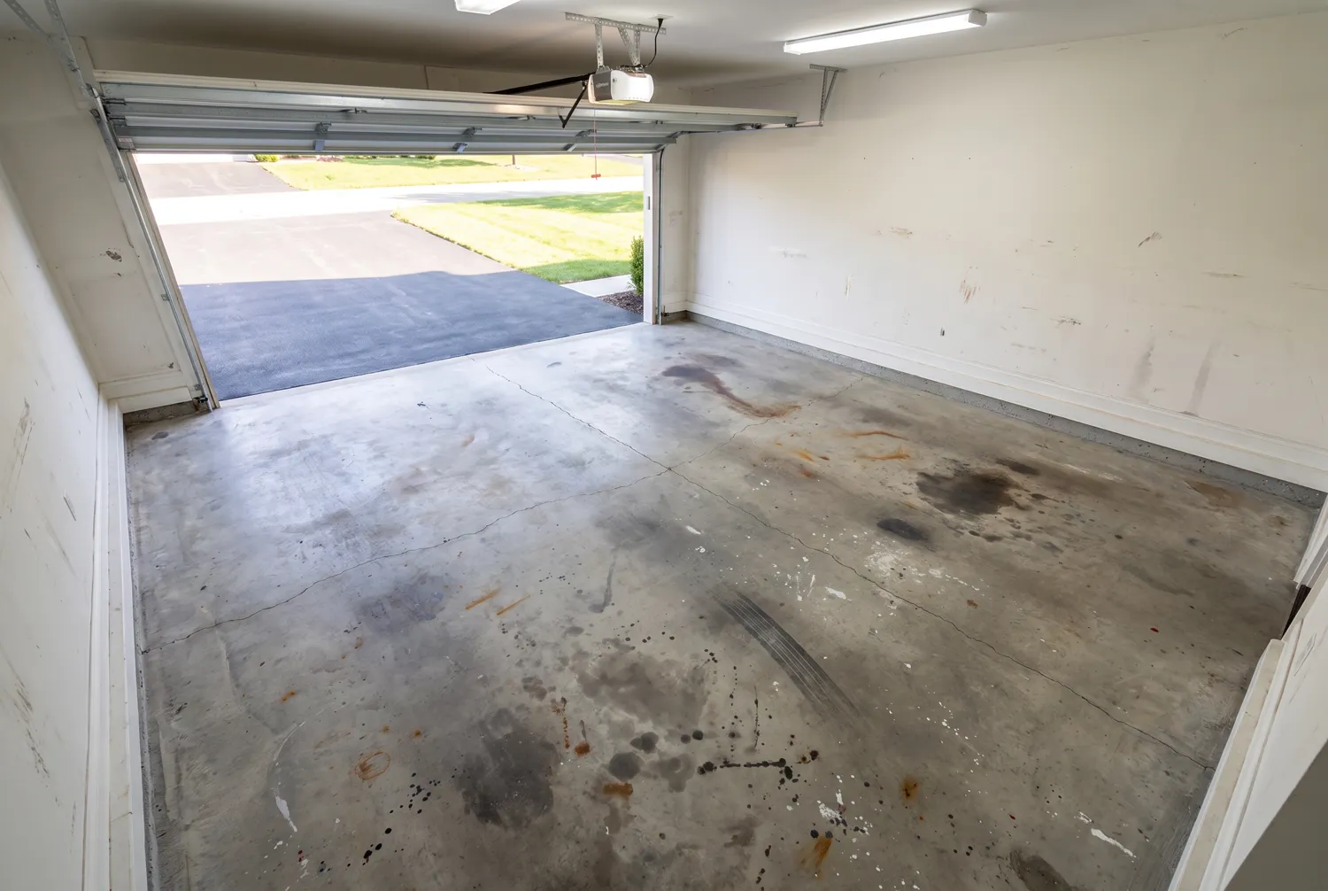 A garage floor before coating, bare concrete with oil stains and a crack