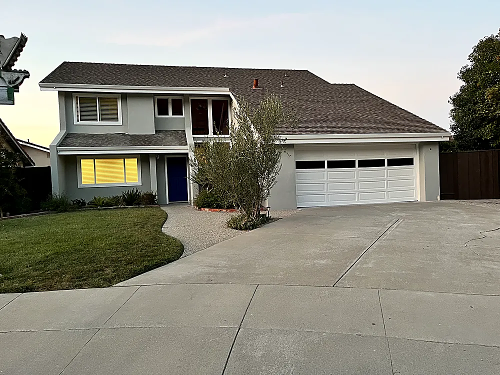 A two story home painted warm grey with a deep blue front door at dusk