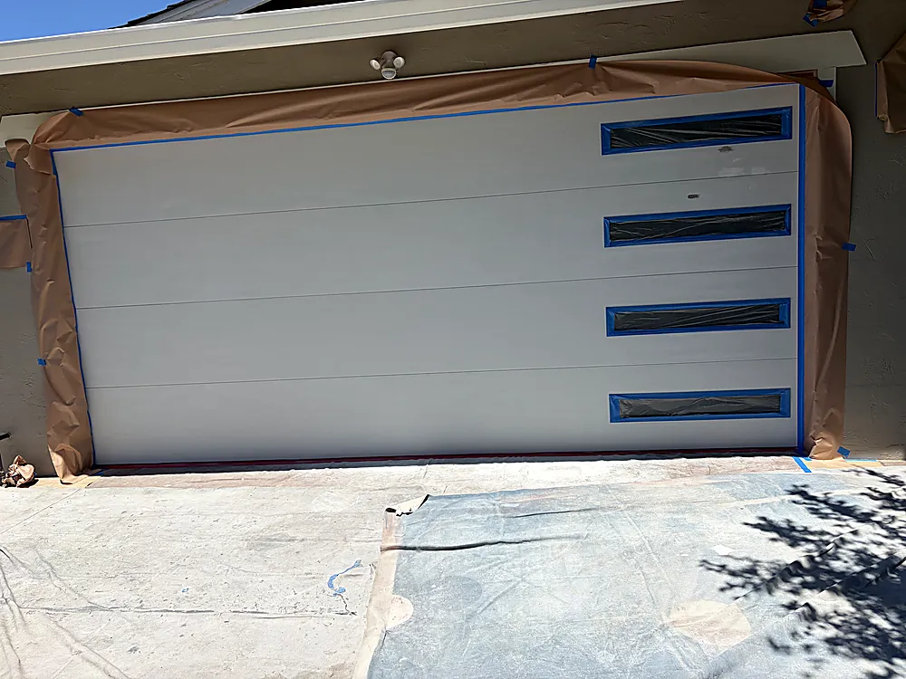 A garage door fully masked with paper and blue tape, primed for its finish coat