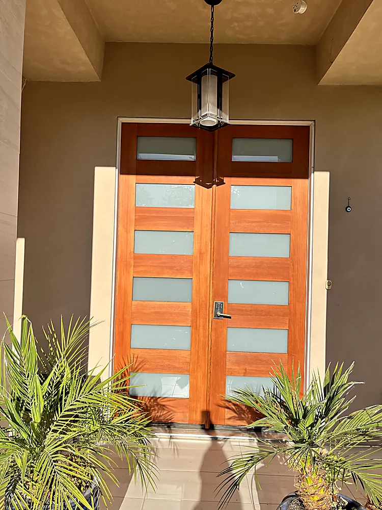 A modern double front door finished in bright orange against cream stucco