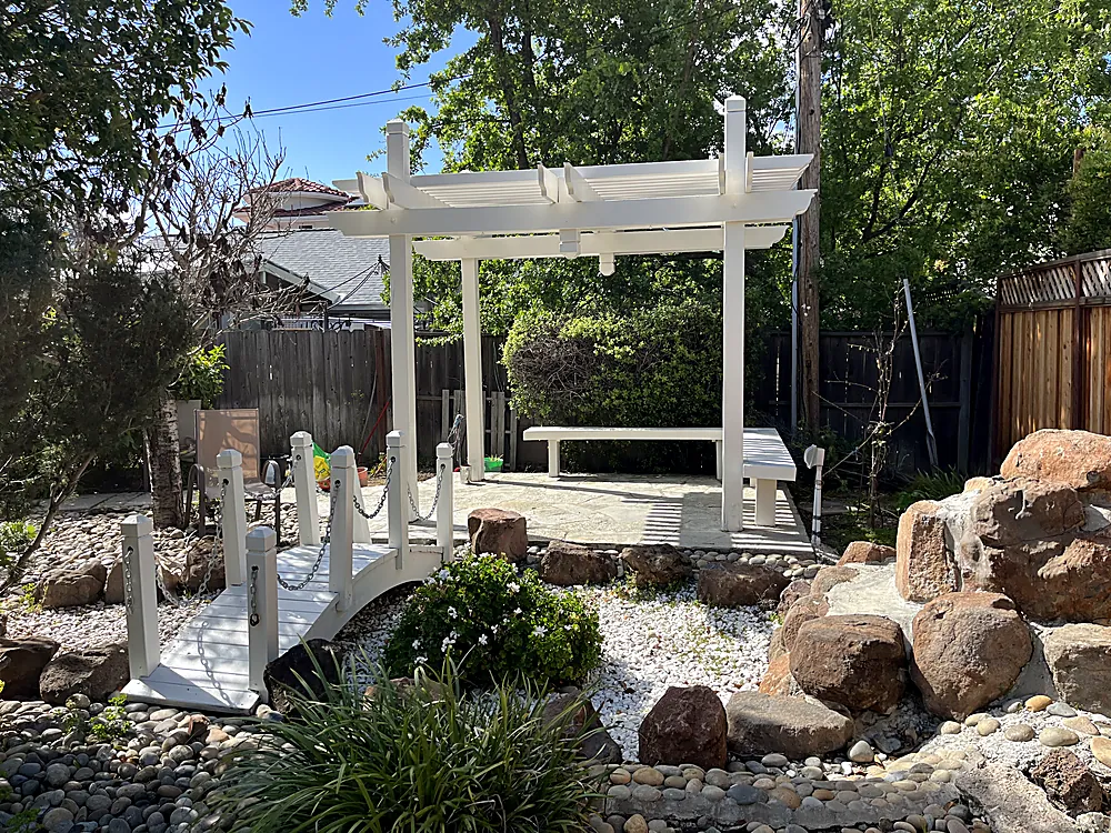 A white pergola and posts beside a rock garden