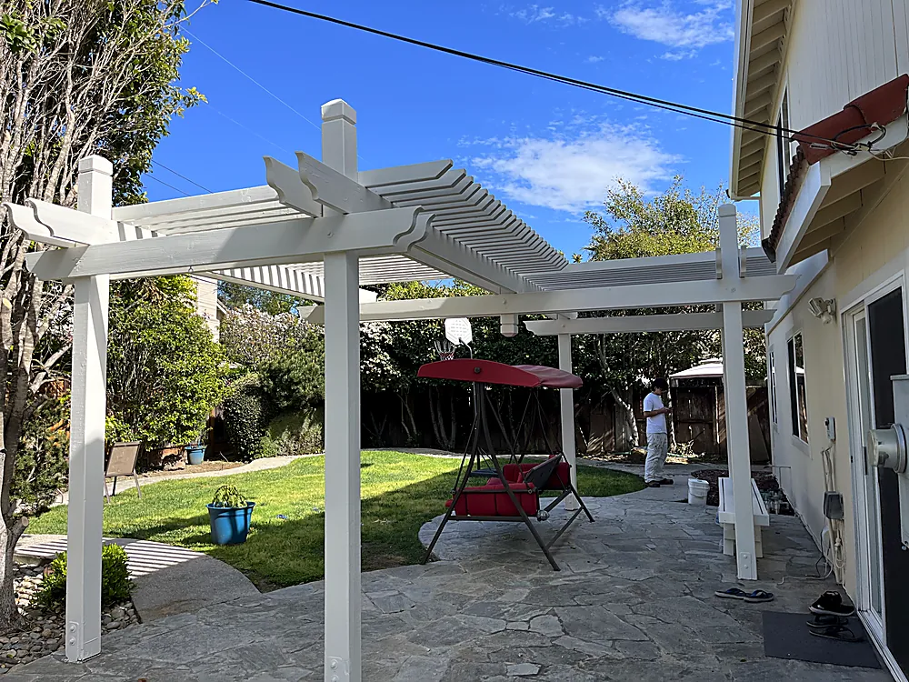 A white painted pergola over a patio beside a home