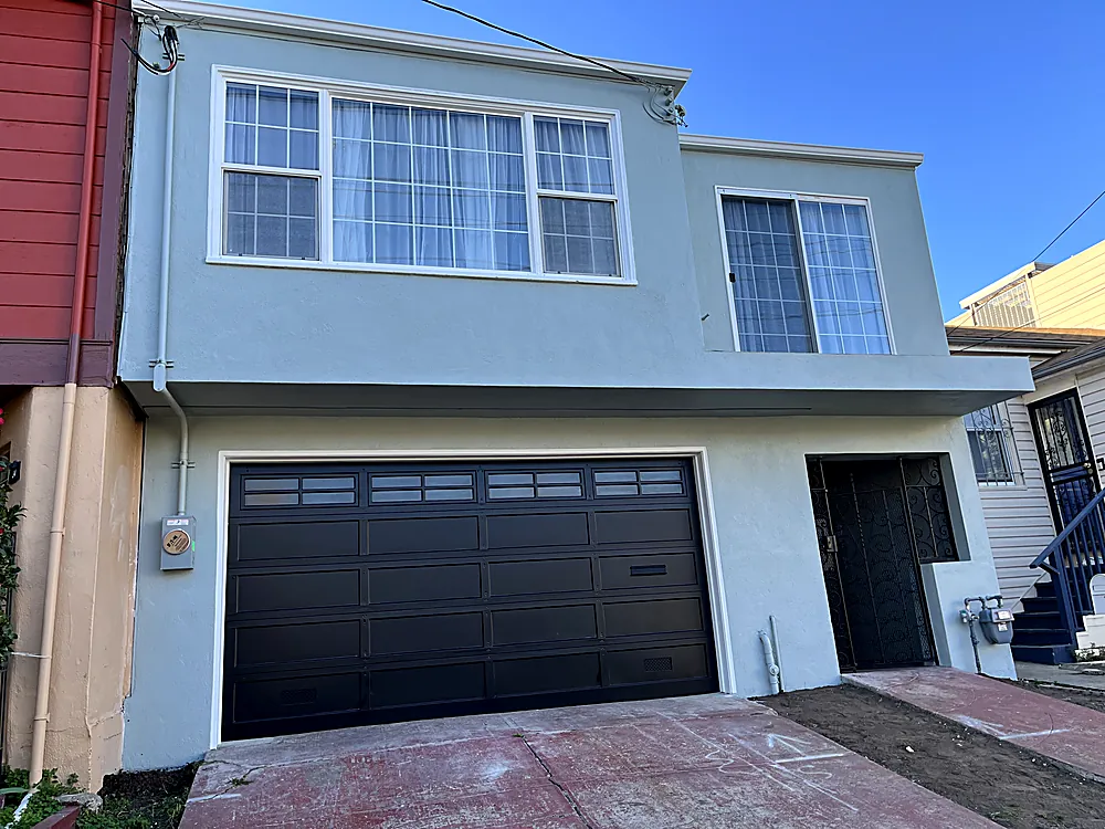 A two story home painted grey blue with white trim and a black garage door