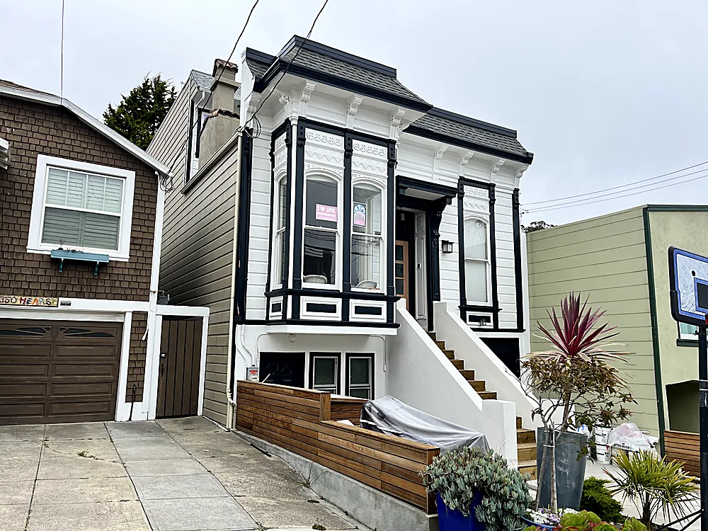 The same white Victorian from a wider angle showing the bay window and entry steps