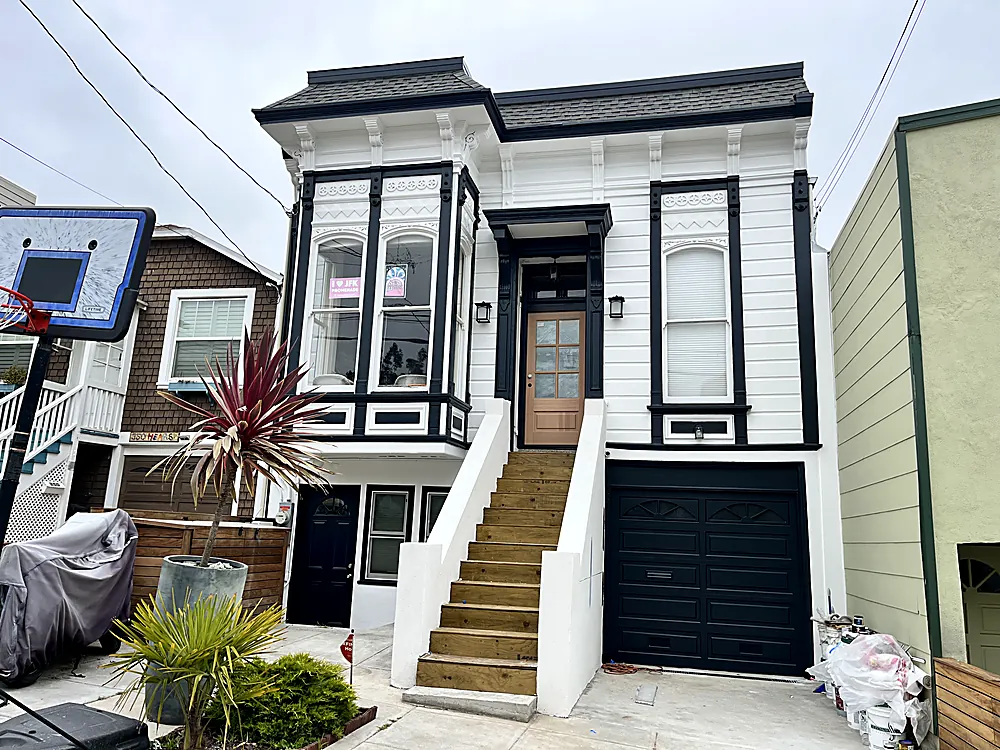 A San Francisco Victorian painted white with black trim and a black garage door