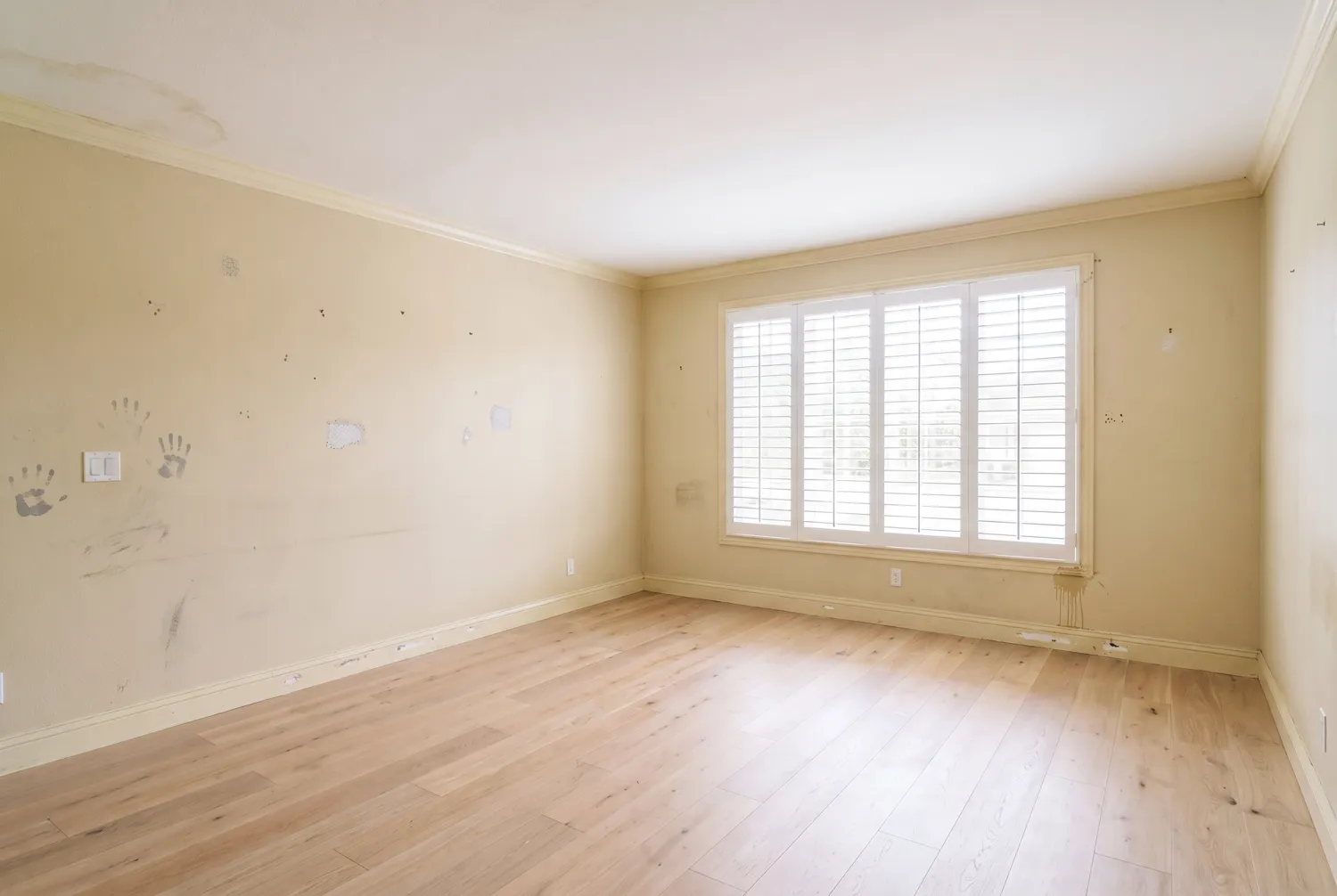 A living room before painting, with dingy yellowed walls, scuffs and nail holes