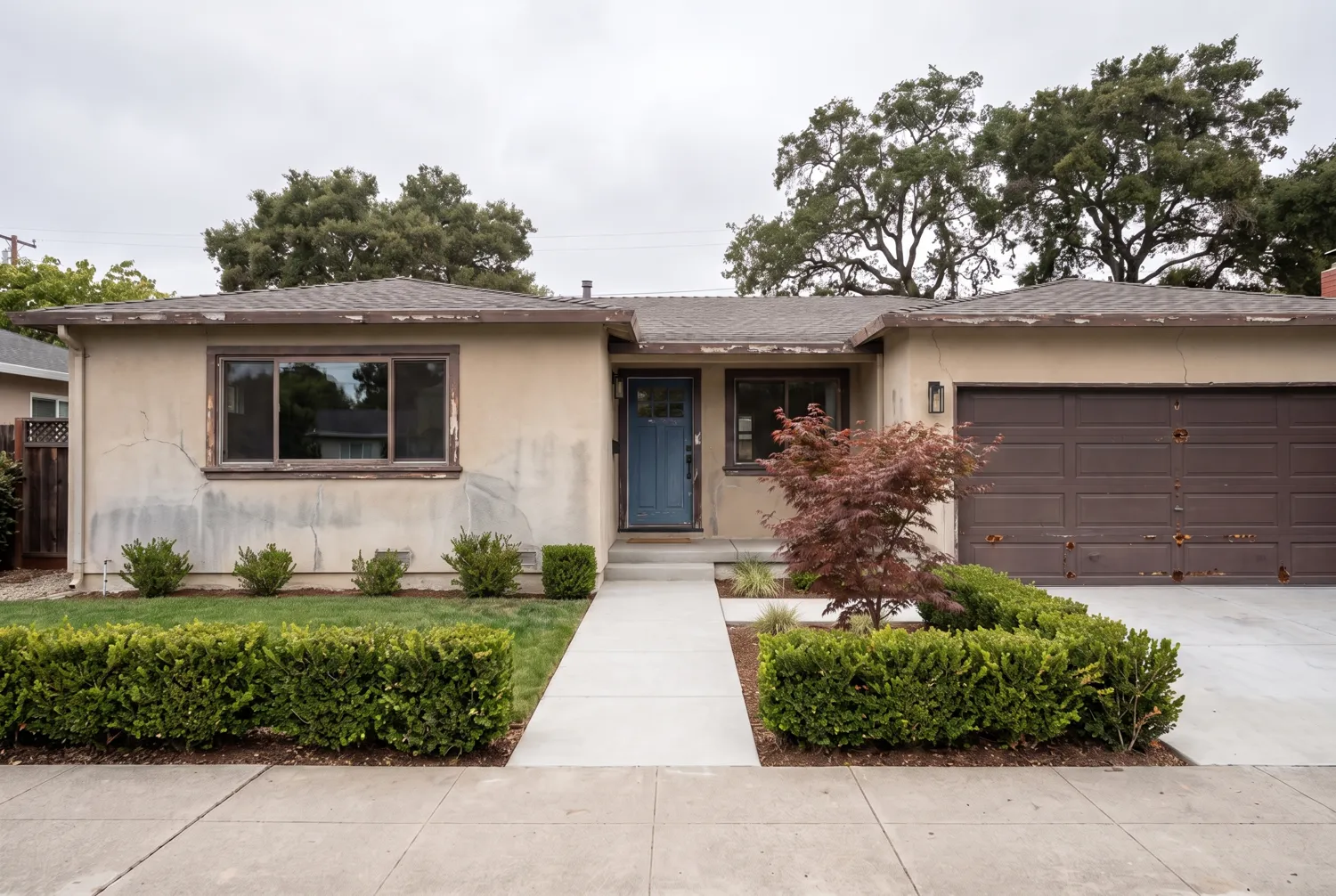 A single story home before painting, with chalky faded stucco and peeling trim